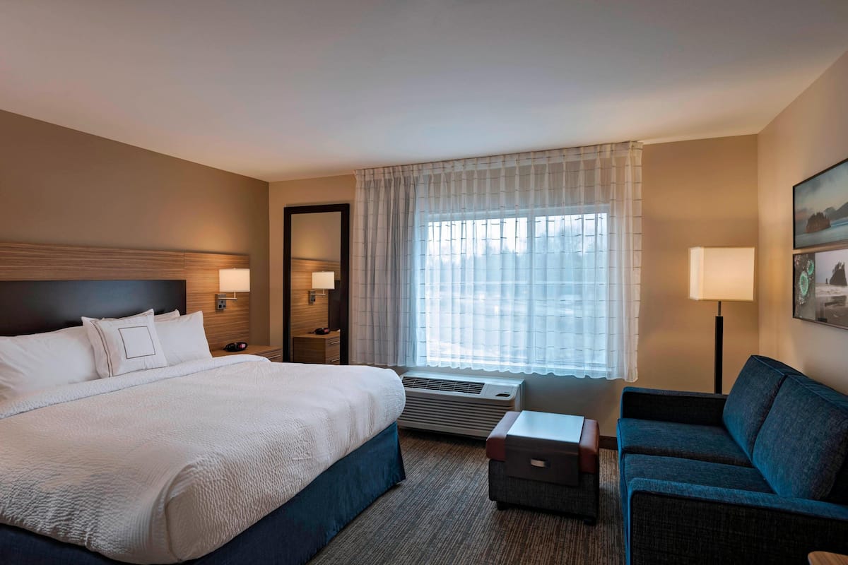 A hotel room with a large bed, a sofa, a desk, and a window with curtains.