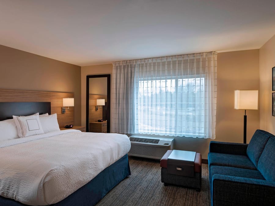 A hotel room with a large bed, a sofa, a desk, and a window with curtains.
