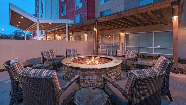 A circular fire pit surrounded by wicker chairs and tables, with a covered patio area and a building in the background. - TownePlace Suites by Marriott Tacoma Lakewood (Lakewood)