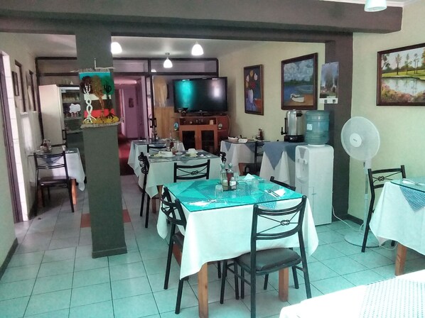 Un comedor con mesas y sillas, un televisor y obras de arte en las paredes.