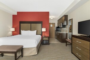 Una habitación de hotel con cama, mesitas de noche, televisor, escritorio y kitchenette.