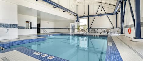 Piscina interior com faixas demarcadas, um boi de salvamento e área de estar com mesas e cadeiras.