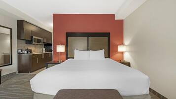 A hotel room with a large bed, a kitchenette, and two bedside lamps.
