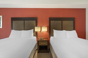 Una habitación de hotel con dos camas, una mesita de noche y una lámpara fijada a la pared.