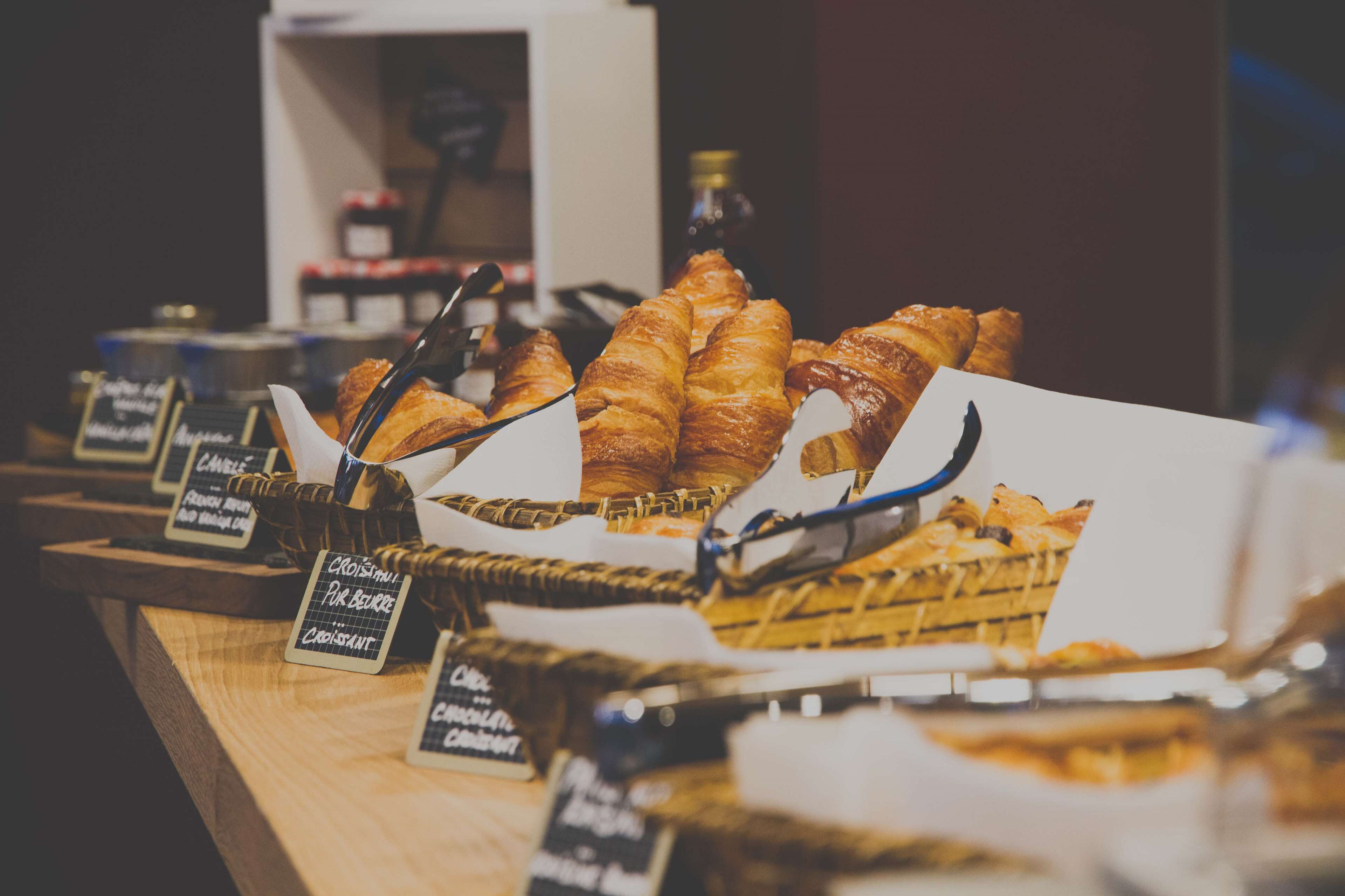 Mostrador de panadería con diversos pasteles y pan, incluyendo croissants y croissants de chocolate, con etiquetas de precio.