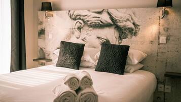 A neatly made bed with rolled towels, two patterned pillows, and a large abstract painting on the wall.