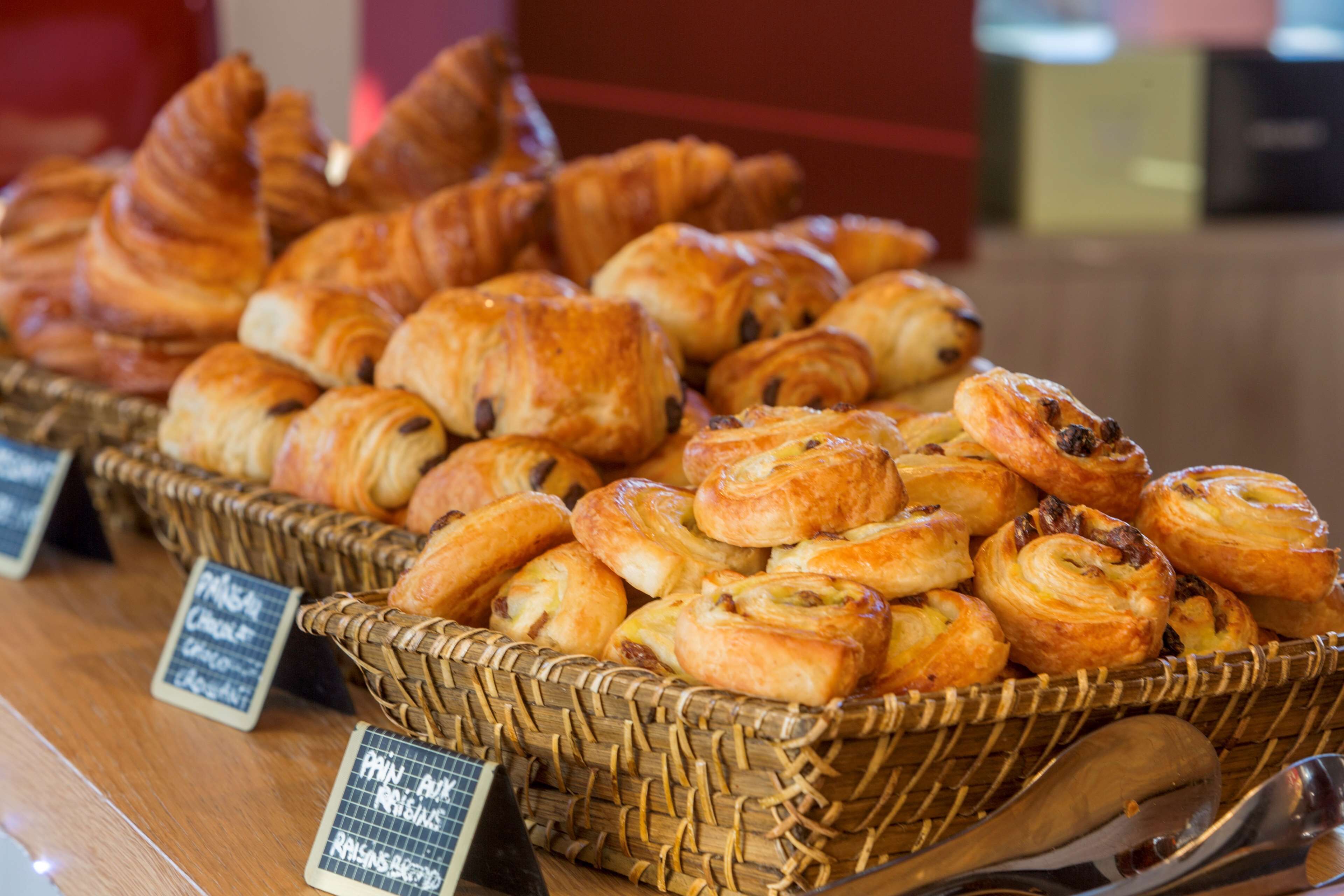 Une variété de pâtisseries présentées dans des paniers en osier, chacun étant accompagné d’une étiquette indiquant le type de pâtisserie.