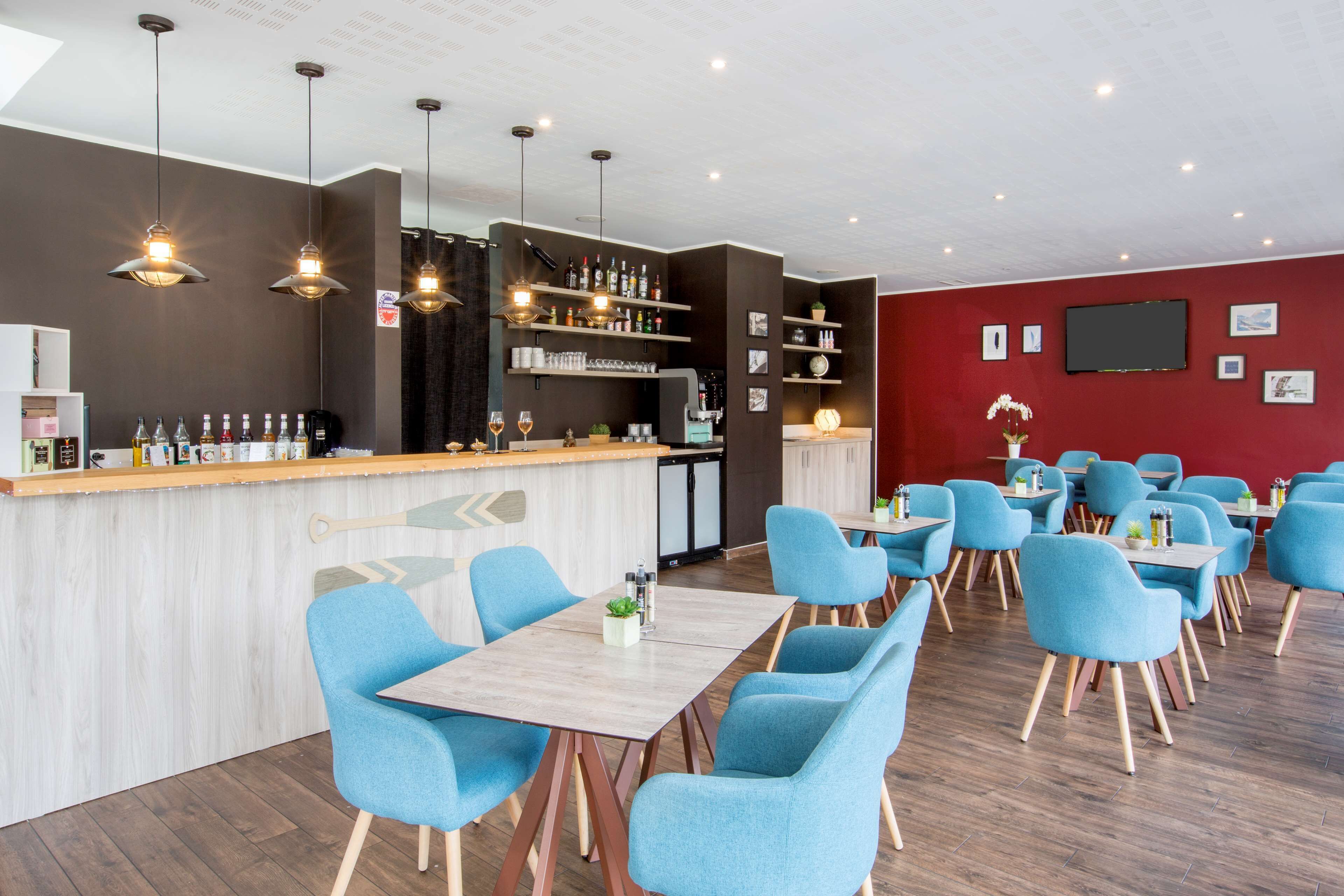 Een modern restaurant met een bar, blauwe stoelen en houten tafels.