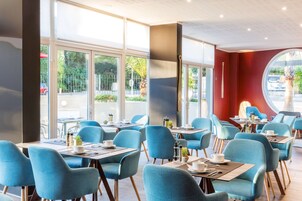 A modern cafe with blue chairs and tables, large windows, and a red accent wall.