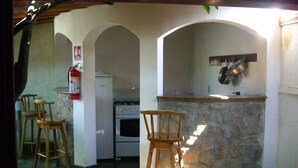 A kitchen with a stone counter, a stove, and a fire extinguisher. There are two wooden chairs and a bar stool.