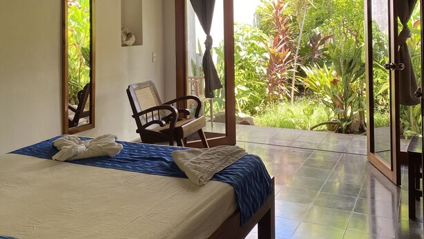 A hotel room with a bed, a chair, a television, a mirror, and a view of the garden.