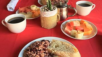 A table set with a variety of dishes including rice, beans, bread, and fruit, along with cups of coffee and a decorative plant.