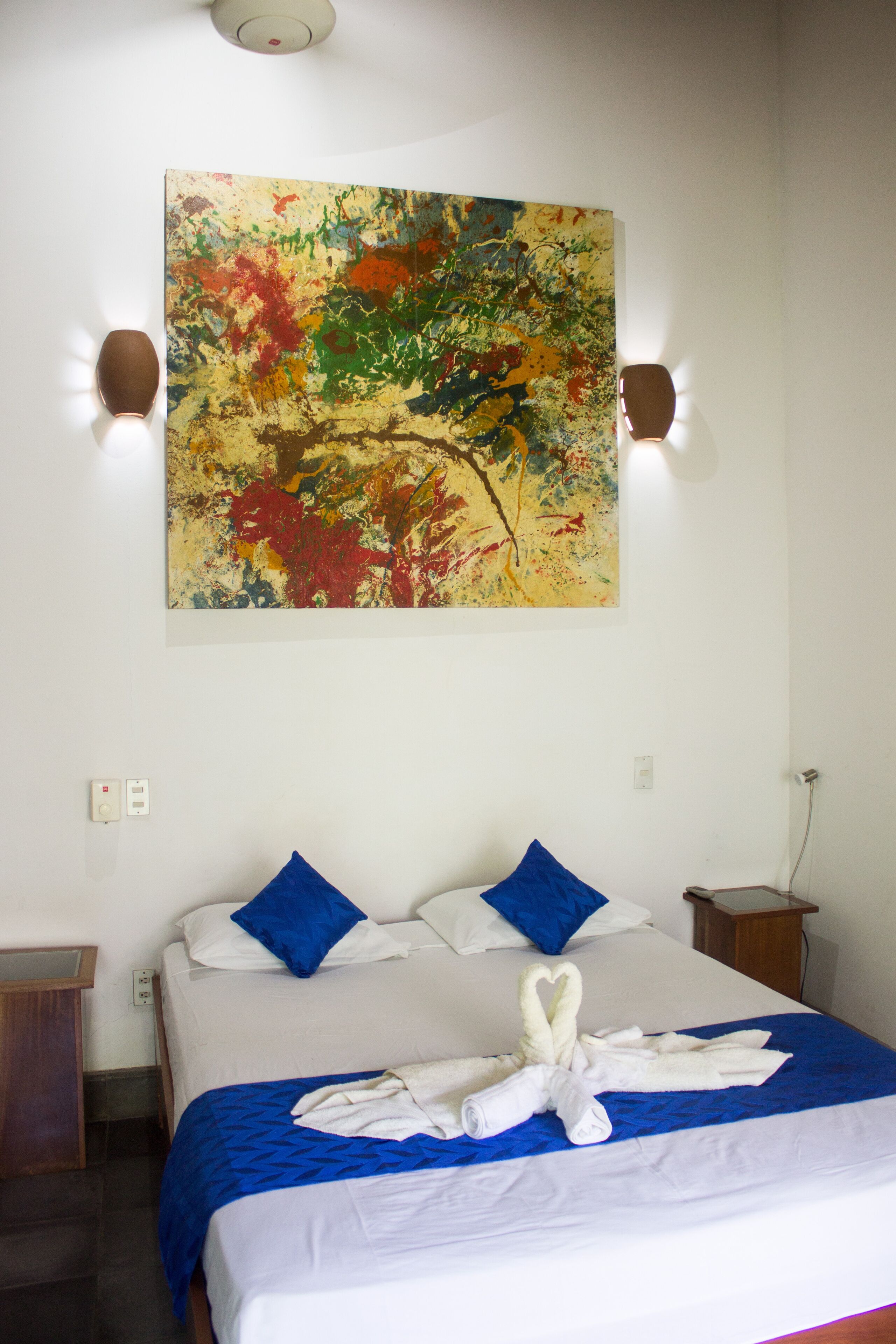 A hotel room with a bed, blue pillows, a white blanket, and a towel art arrangement.