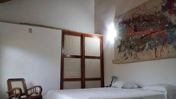 A bedroom with a bed, a chair, a wardrobe, and a large abstract painting on the wall.