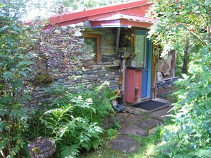 A rustic stone building with a red roof, a wooden door, and a small porch area. - Brigitte's Bavarian B&B (Homer)