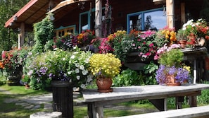 A wooden cabin with a porch adorned with colorful flower arrangements and a stone pathway leading to the entrance. - Brigitte's Bavarian B&B (Homer)