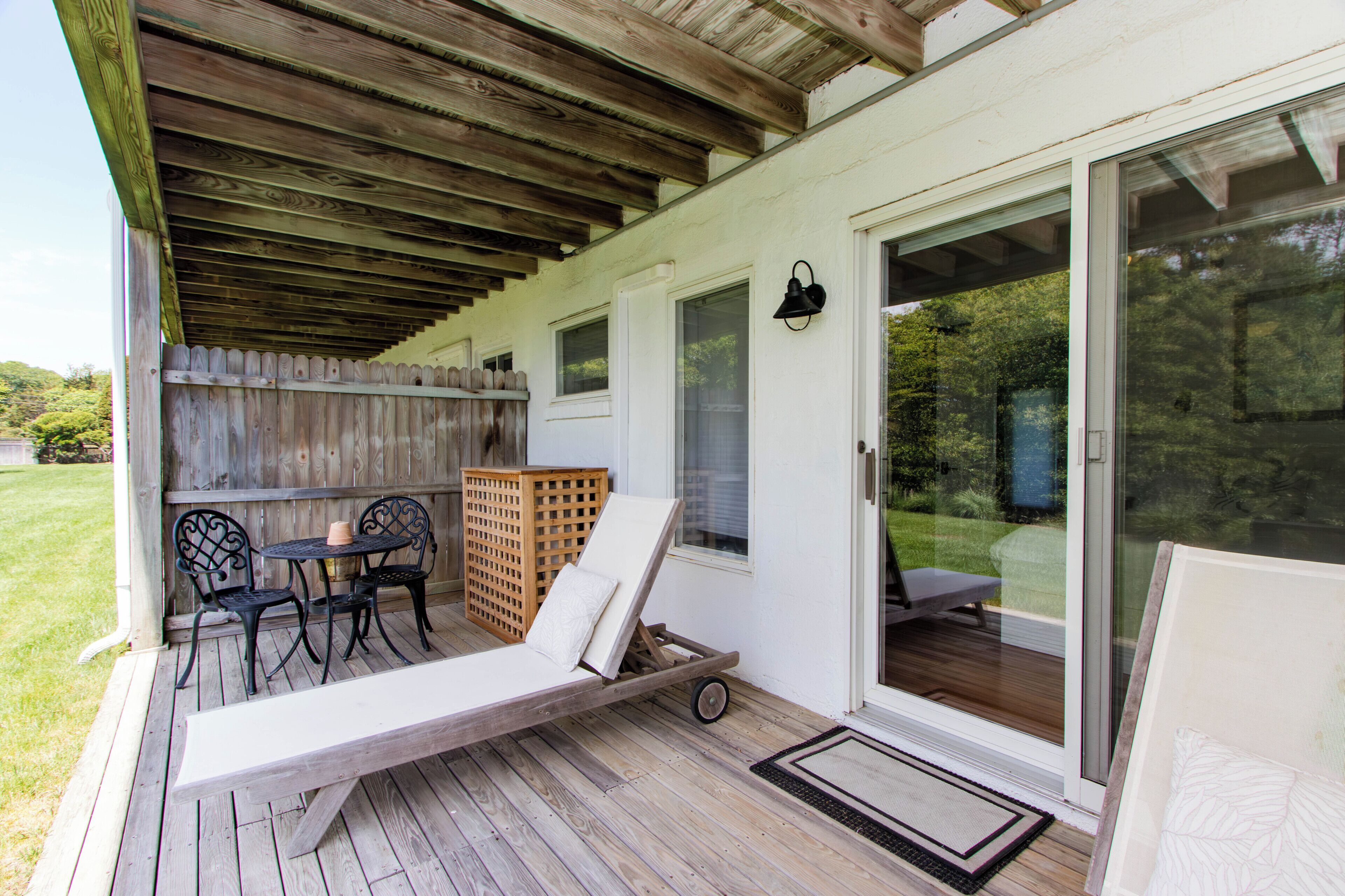 Een overdekt terras met een houten terras, één loungestoel, een bijzettafeltje en een houten schutting.