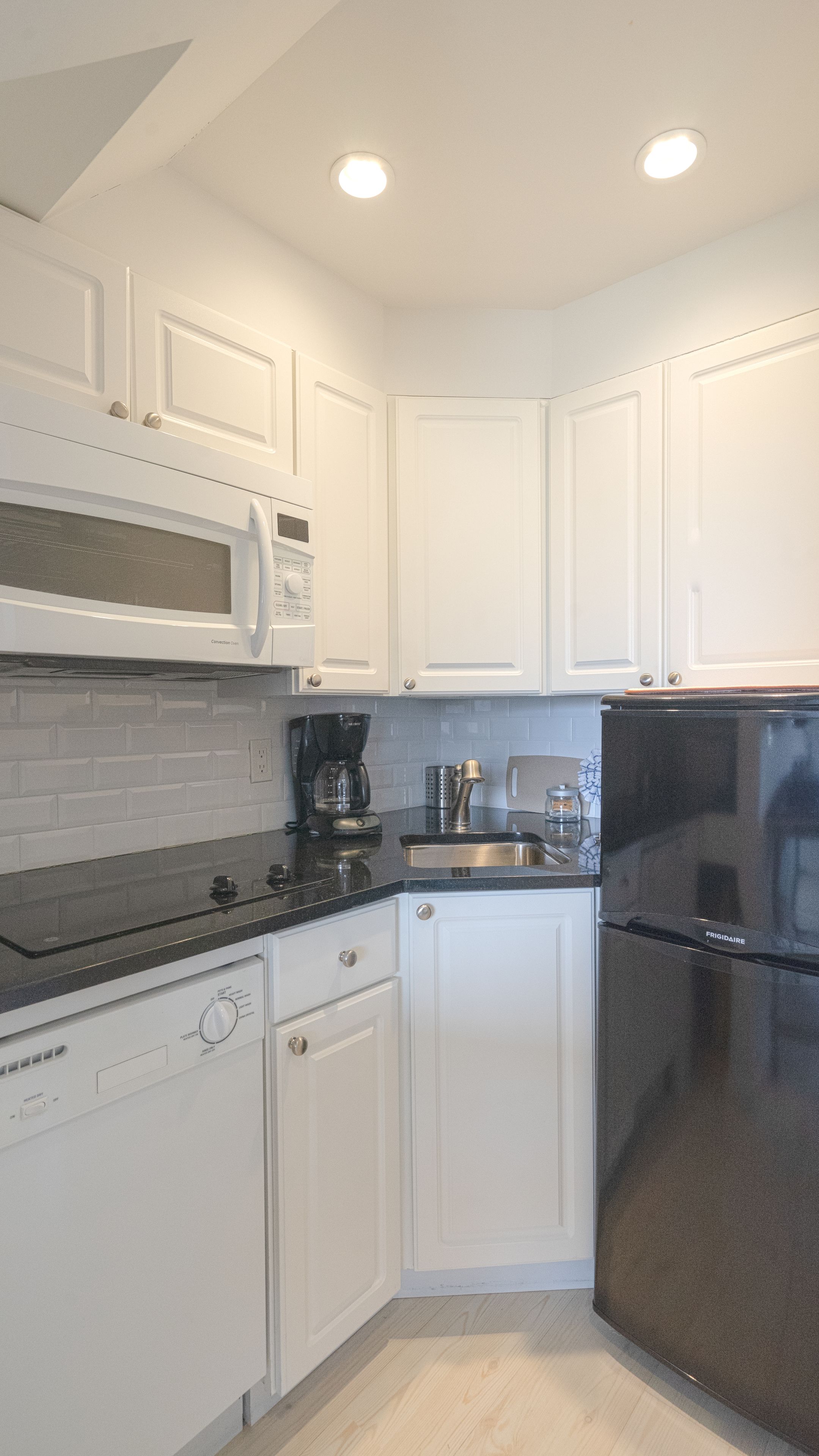 A compact kitchen with white cabinetry, a black refrigerator, a microwave, a coffee maker, and a dishwasher.
