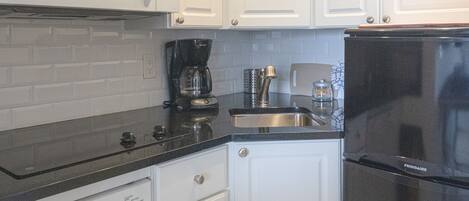 A compact kitchen with white cabinetry, a black refrigerator, a microwave, a coffee maker, and a dishwasher.