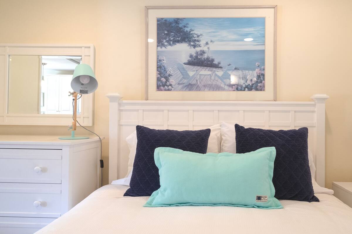 Een slaapkamer met een bed, twee nachtkastjes, een dressoir, een spiegel en een ingelijst schilderij aan de muur.