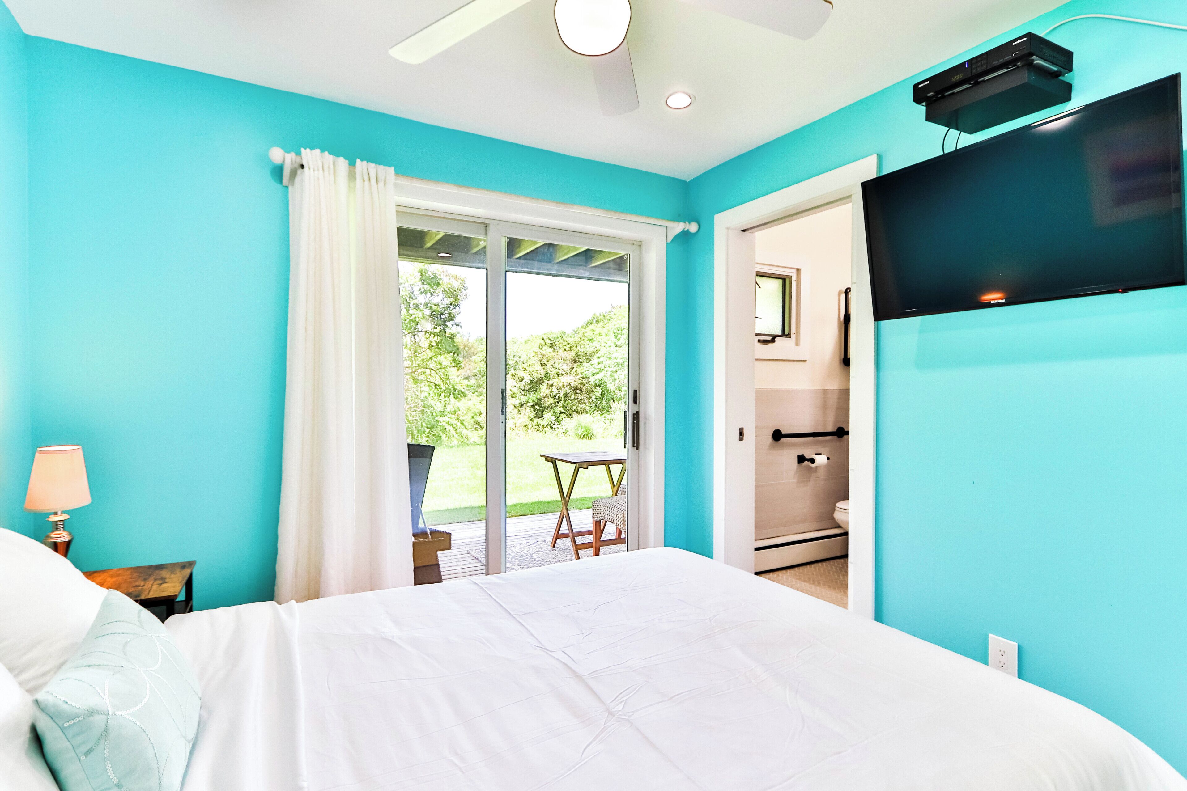 Une chambre à coucher avec un lit, un téléviseur fixé au mur et une porte-fenêtre coulissante donnant sur un espace extérieur.