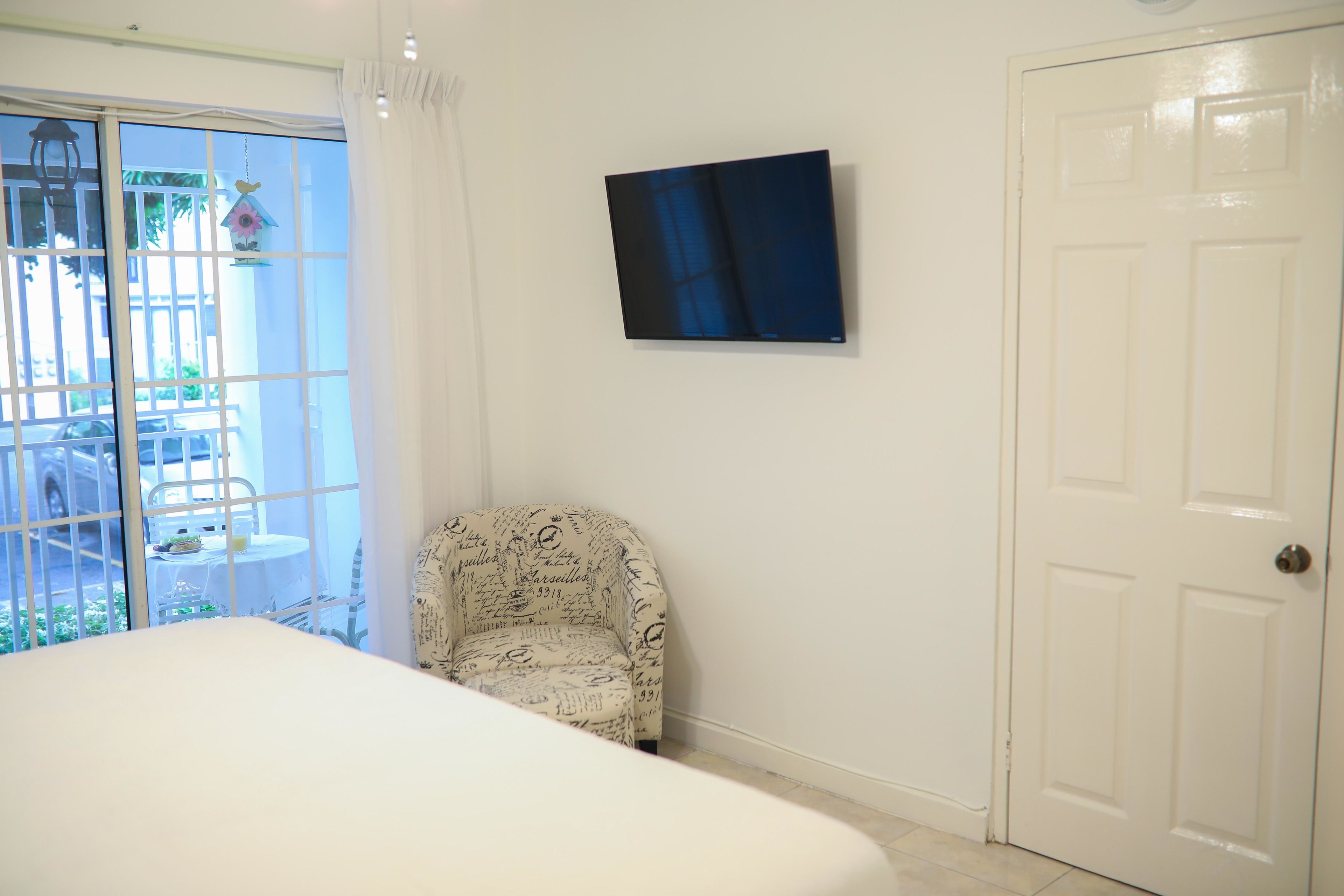Une chambre avec un lit, une chaise, un téléviseur fixé au mur et une porte.