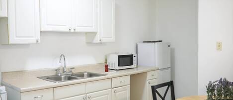 A kitchen with white cabinets, a microwave, a sink, and a refrigerator.