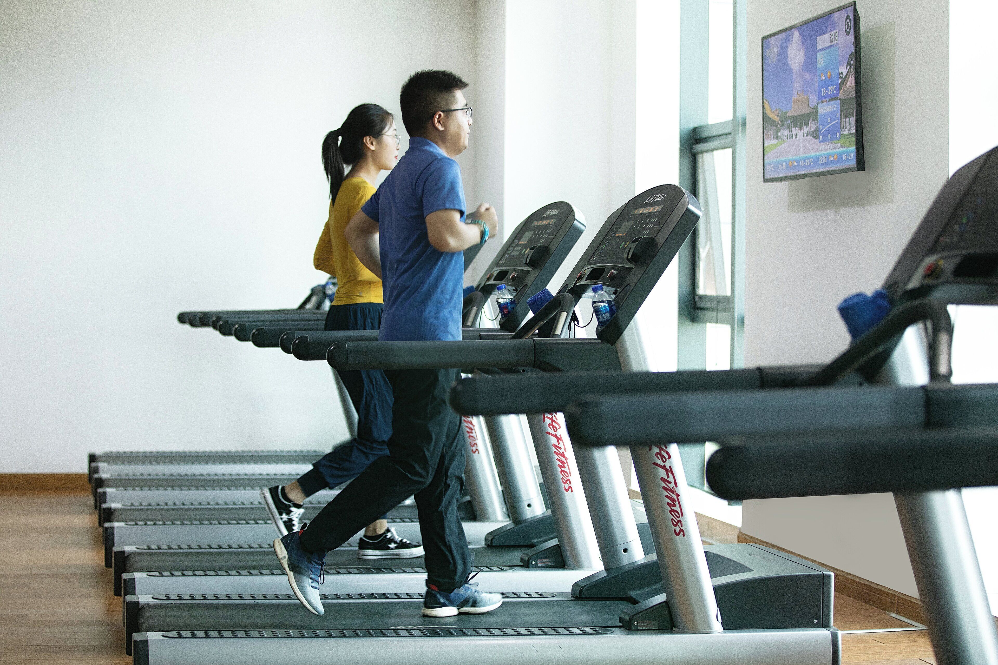 A gym with treadmills lined up against a wall, a water bottle on one of the machines, and a poster on the wall.