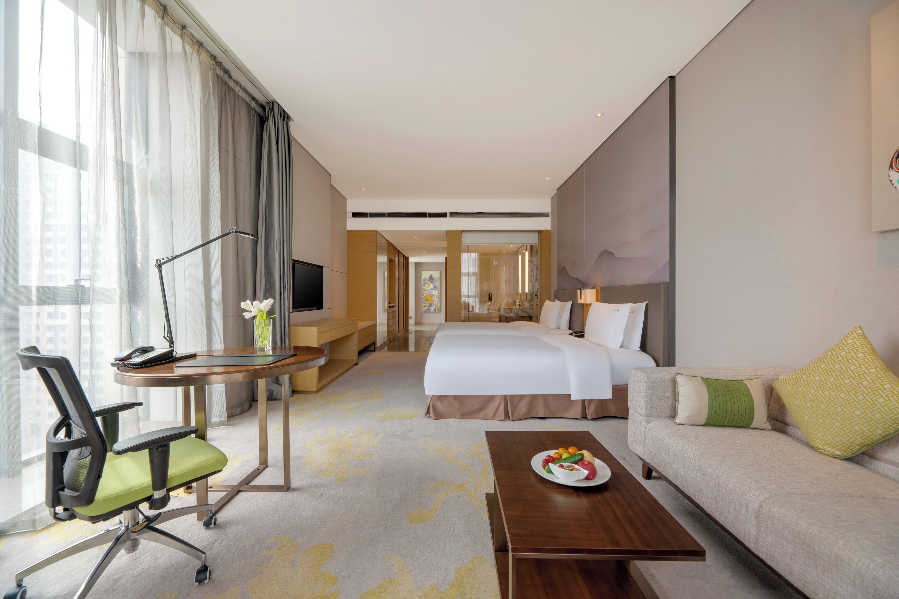 Une chambre d’hôtel comprenant un lit, un canapé, un bureau avec une chaise, une télévision et une table à manger avec une assiette de fruits.