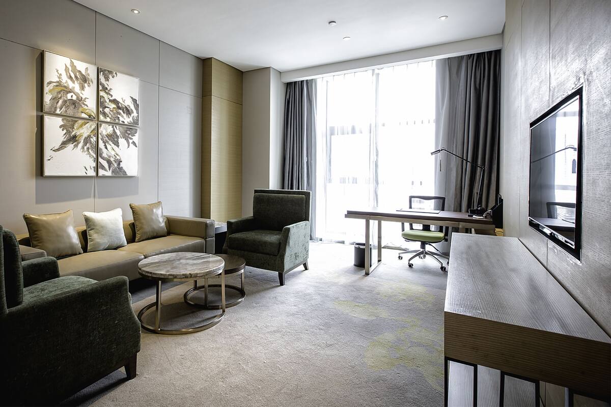 Une chambre d’hôtel moderne équipée d’un canapé, de fauteuils, d’une petite table basse, d’un bureau et d’une télévision.