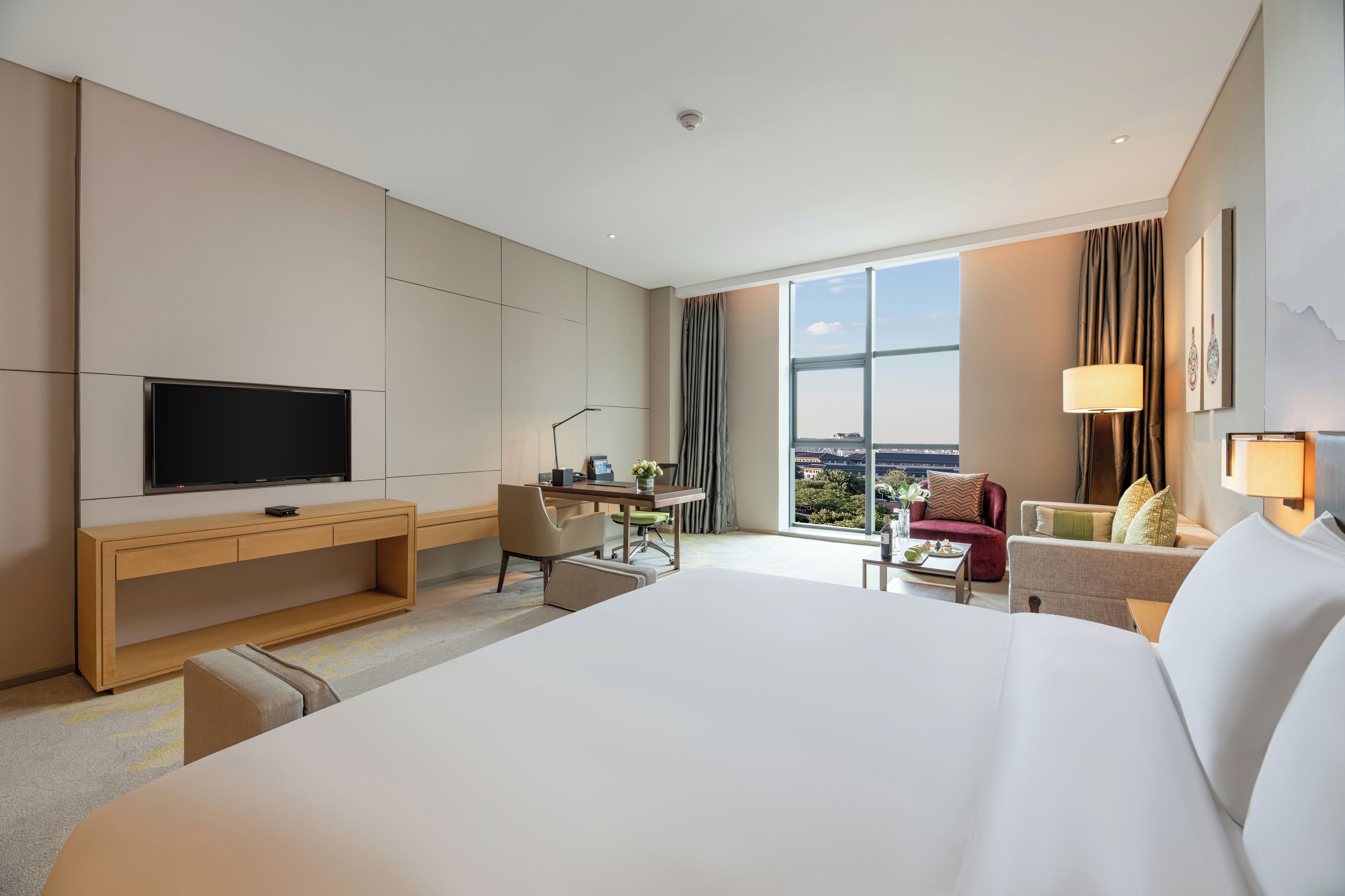 A hotel room with a large bed, a desk with a chair, a television, and a view of the city.