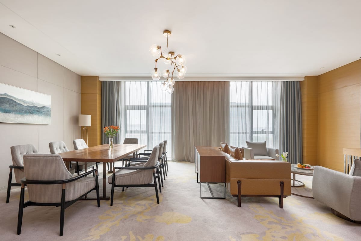 Une chambre d’hôtel moderne dotée d’un coin repas, d’un ensemble de canapés, d’une télévision et d’une grande fenêtre avec des rideaux.