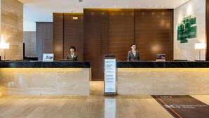 A reception desk with two staff members, a signboard, and a logo on the wall. - Holiday Inn Baoji Central by IHG (Baoji)