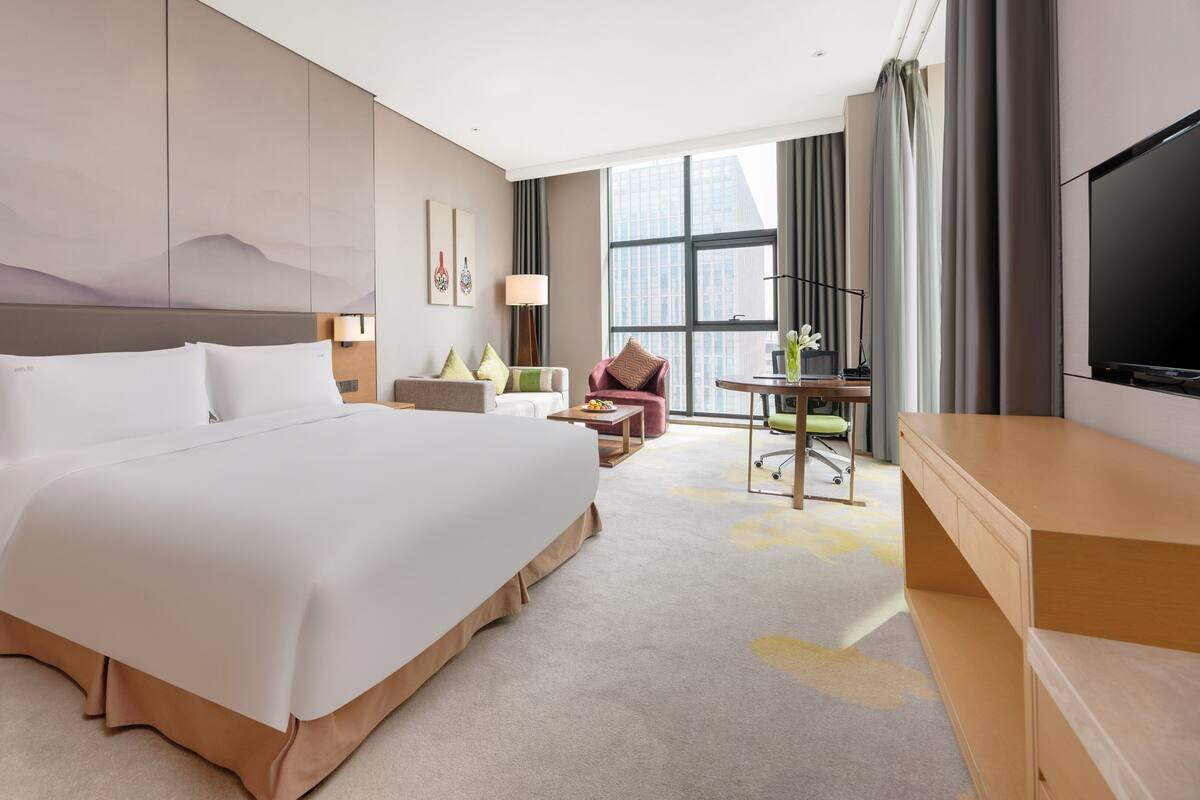 Une chambre d’hôtel avec un grand lit, un bureau avec une chaise, une télévision et une fenêtre avec des rideaux.