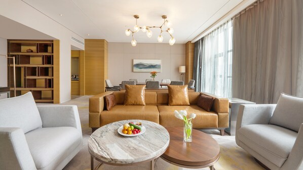 A modern living room with a brown leather sofa, two grey armchairs, a marble coffee table, and a dining area with a table and chairs. - Holiday Inn Baoji Central by IHG (Baoji)
