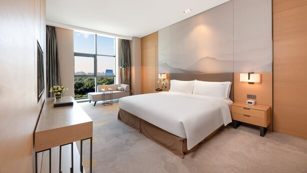 Ein modernes Hotelzimmer mit einem großen Bett, Nachttischen, einem Schreibtisch und Blick auf die Stadt.