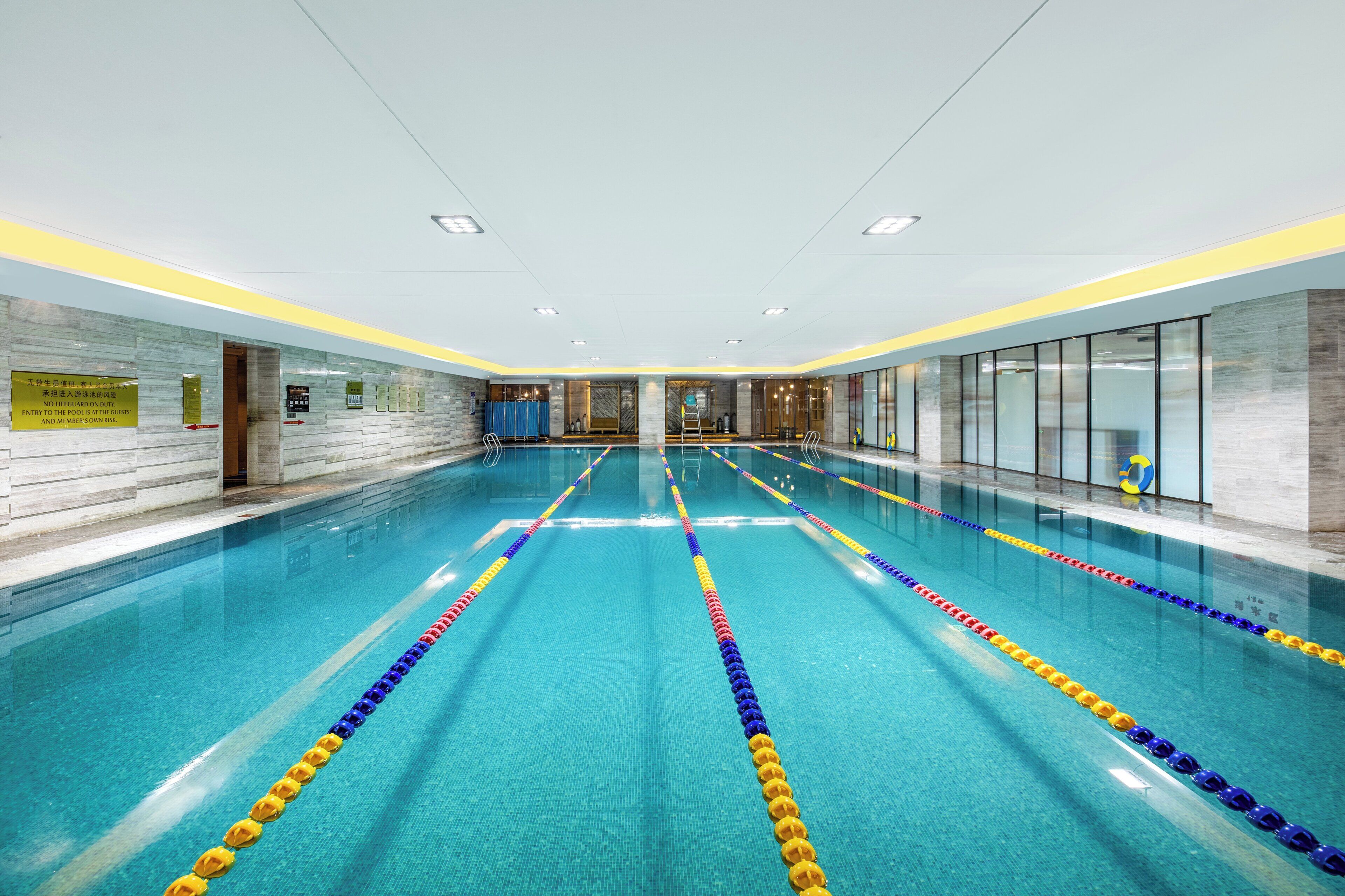 Una amplia piscina interior con carriles delimitados, pared de azulejos y techo luminoso.