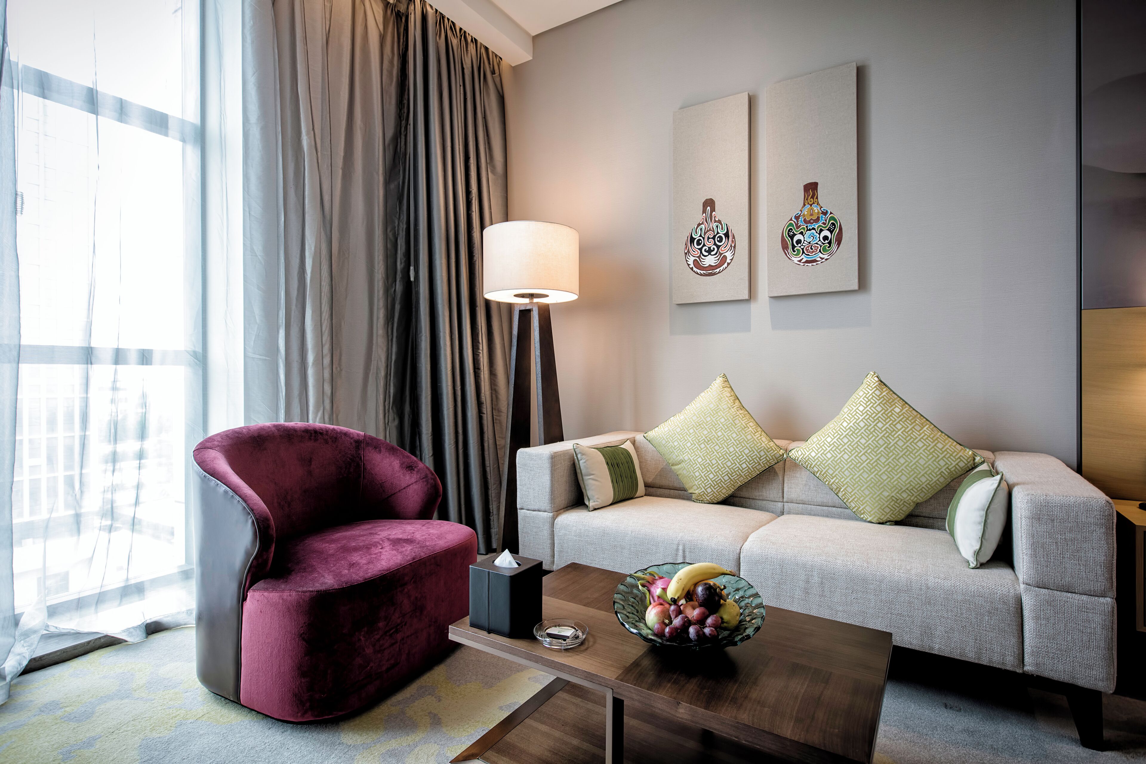 Una sala de estar moderna con un sillón rojo, un sofá gris con cojines estampados, una mesa de centro con frutero y una lámpara de pie.