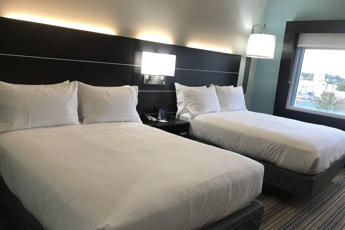 Ein Hotelzimmer mit zwei Betten, einem Nachttisch, einer Lampe und einem Fenster mit Blick.