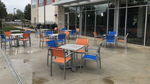 Un espace extérieur aménagé en terrasse avec des tables et des chaises, un bâtiment doté de grandes fenêtres et un ciel dégagé.