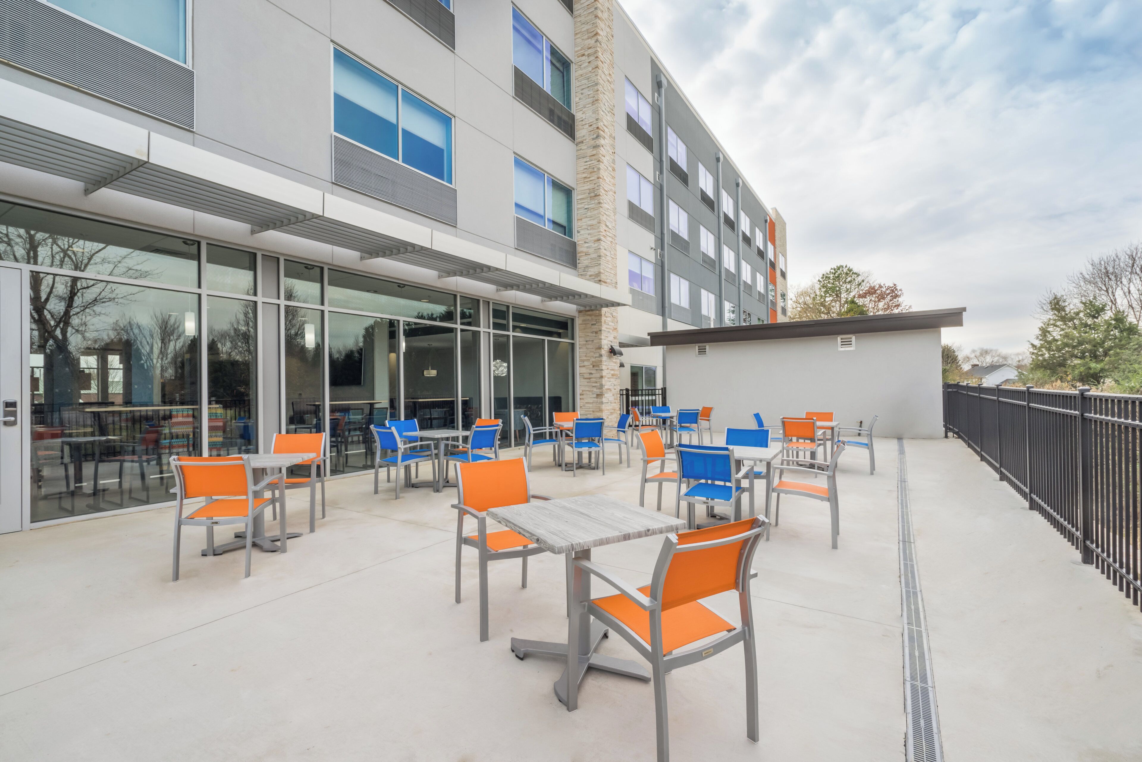 An outdoor patio area with tables and chairs, a building with large windows, and a clear sky.