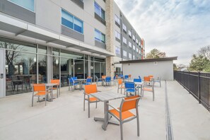 Un espace extérieur aménagé en terrasse avec des tables et des chaises, un bâtiment doté de grandes fenêtres et un ciel dégagé.