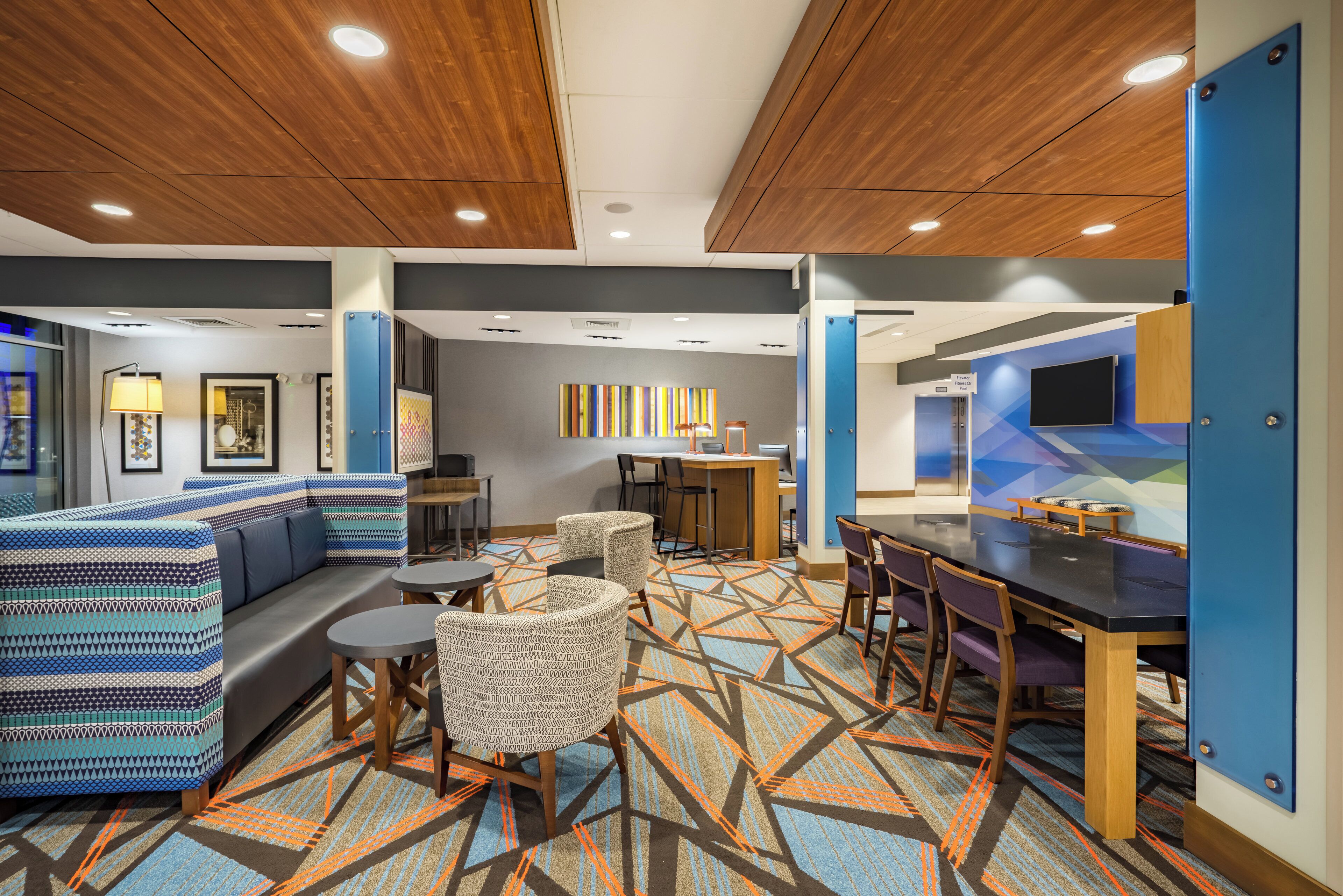A modern hotel lobby with a seating area, a reception desk, and a fitness center sign.