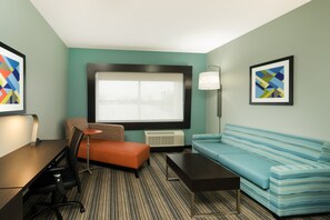 Ein modernes Hotelzimmer mit großem Fenster, einer Couch, einem kleinen Tisch und einem Schreibtisch mit Stuhl.