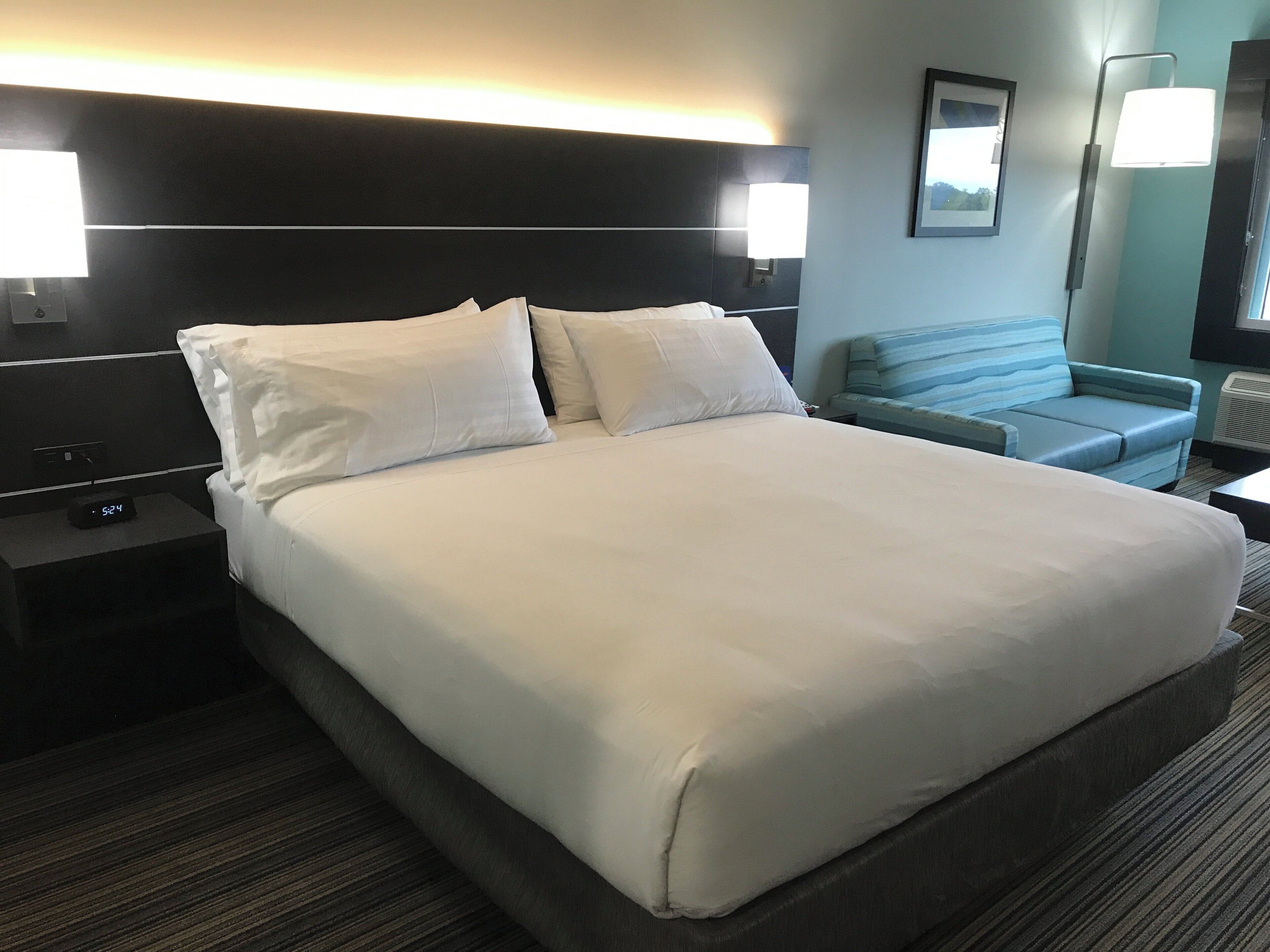 Ein Hotelzimmer mit einem großen Bett, zwei Nachttischen, einem Sofa und einer stehenden Lampe.