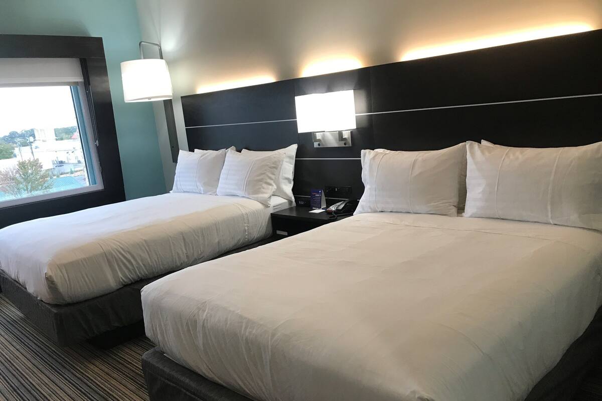 Ein Hotelzimmer mit zwei Betten, einem Nachttisch mit Telefon und einem Fenster mit Blick auf Gebäude.