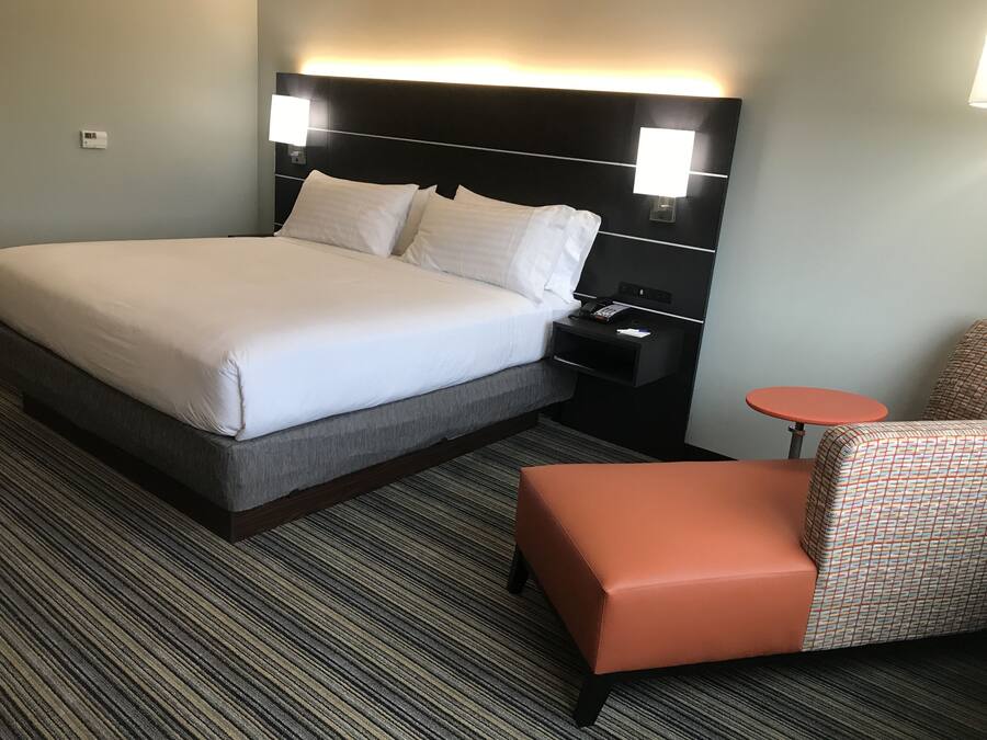 Una habitación de hotel con cama, mesita de noche, silla y una pequeña mesa.