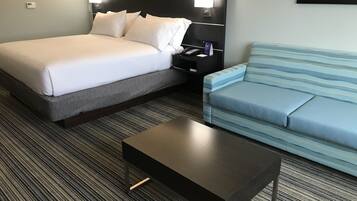 Una habitación de hotel con cama, mesita de noche, lámpara, sofá y una mesa de centro.