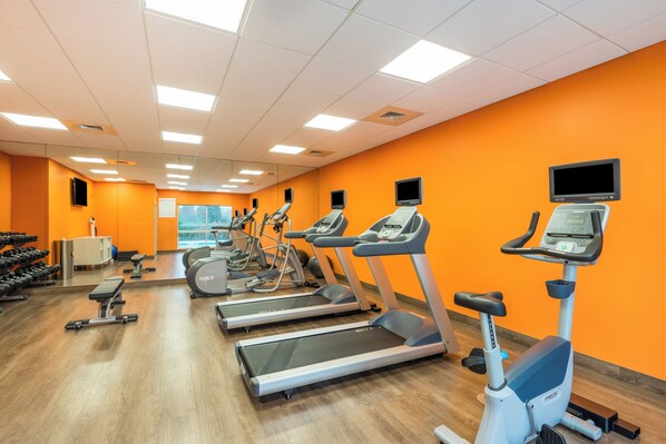 Une salle de sport équipée de tapis de course, de vélos elliptiques et de poids libres.