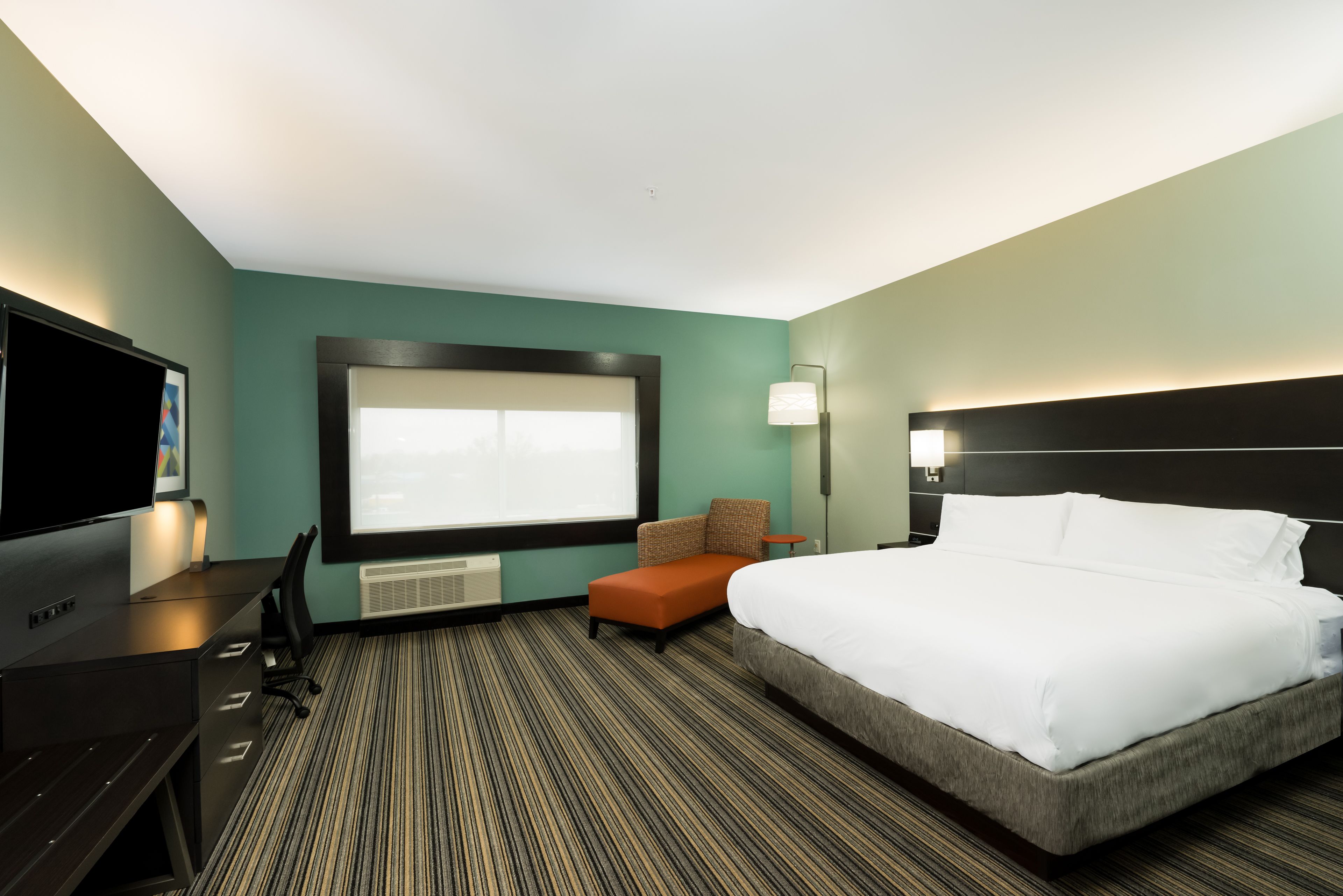 Habitación de hotel con una cama grande, un escritorio con computadora, una silla y una ventana con persianas.